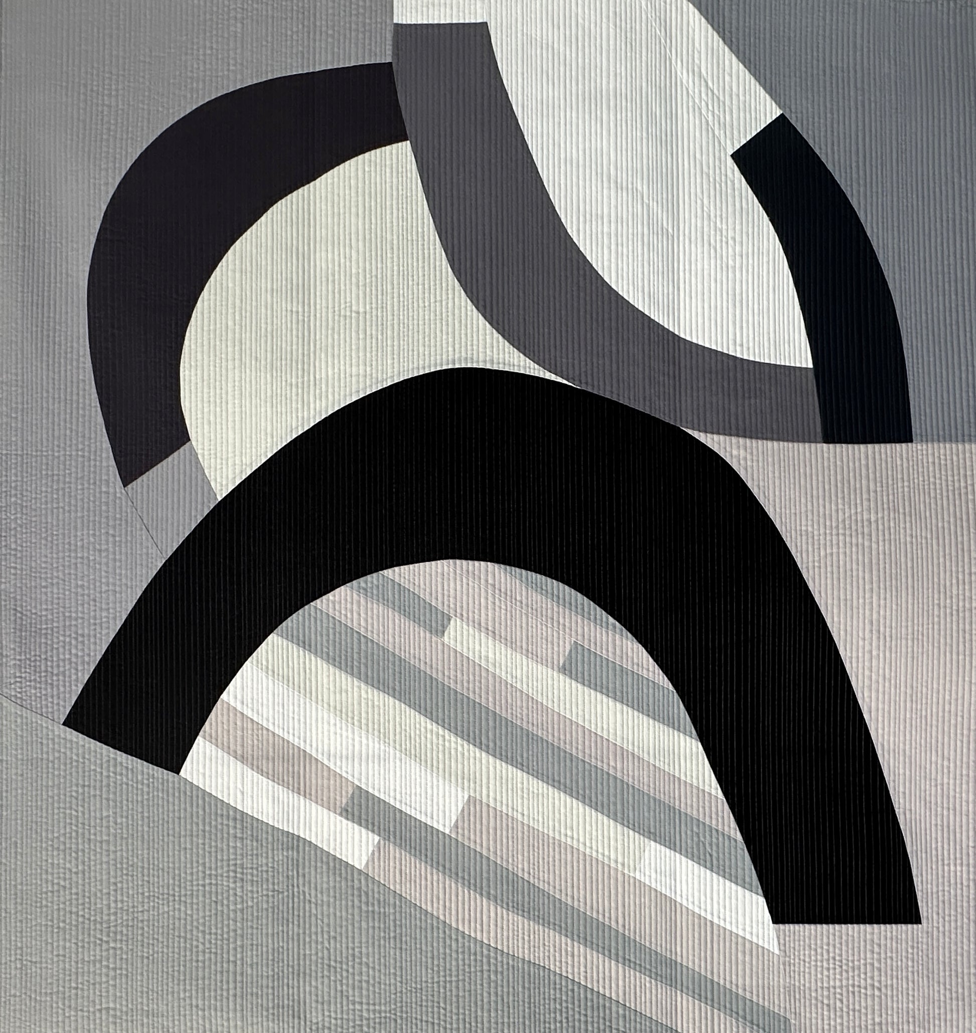 Abstract art quilt with black and white curved shapes on a textured gray background
